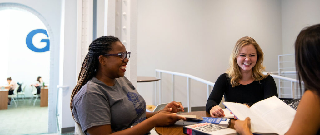 Group of three graduate students sitting and talking around a table in the Car Barn graduate student lounge.